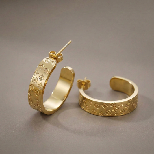 Engraved gold hoop earrings with gold butterfly backs on a softly lit warm-gray background.