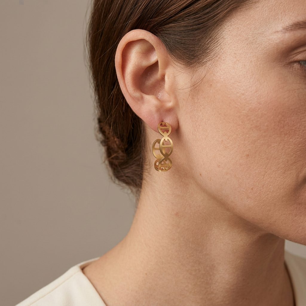 Model wearing a gold openwork D-motif hoop earring in an eye-free close-up against a warm-gray background.