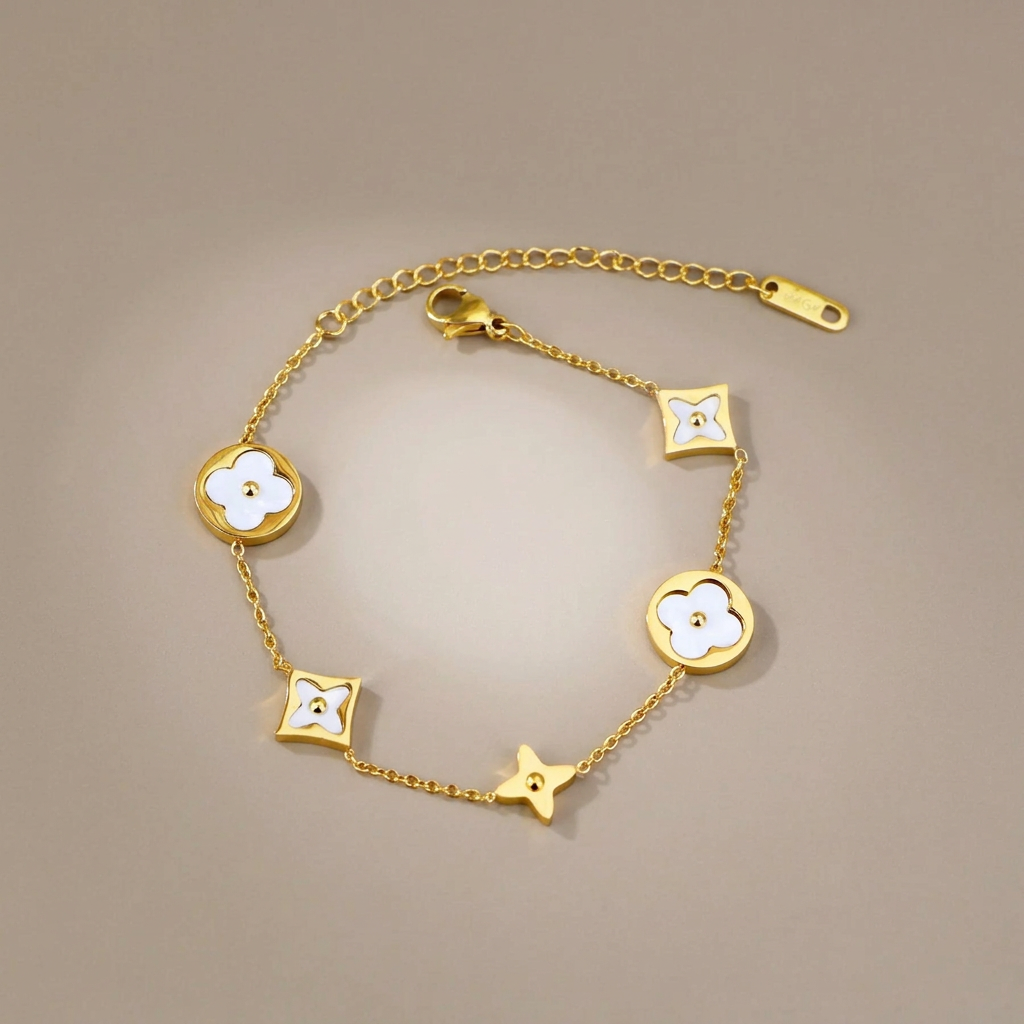 Gold mother-of-pearl clover bracelet arranged on a softly lit warm-gray studio background.