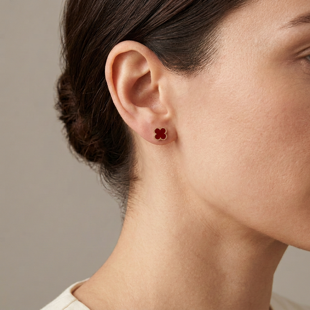 Red clover stud earring with gold-tone beaded edging worn by a model against a warm gray background