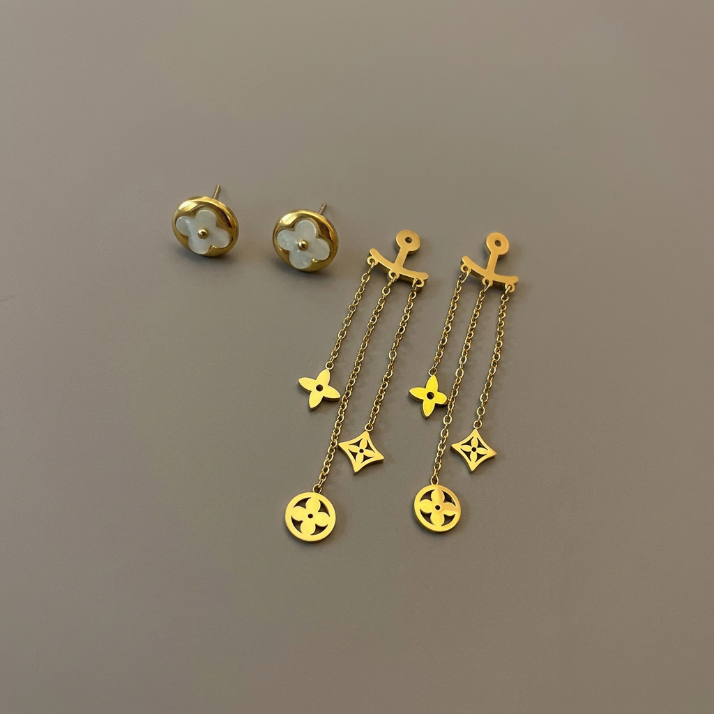 Mother-of-pearl clover studs and separate gold dangling ear jackets displayed on a warm-gray background.