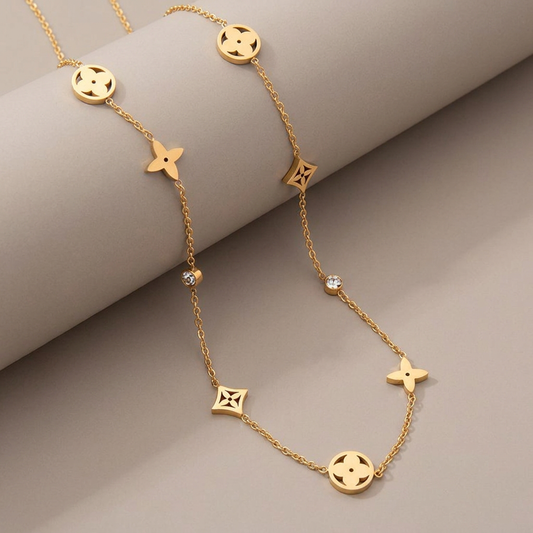 Gold clover charm necklace with CZ accents on a warm-gray studio background.