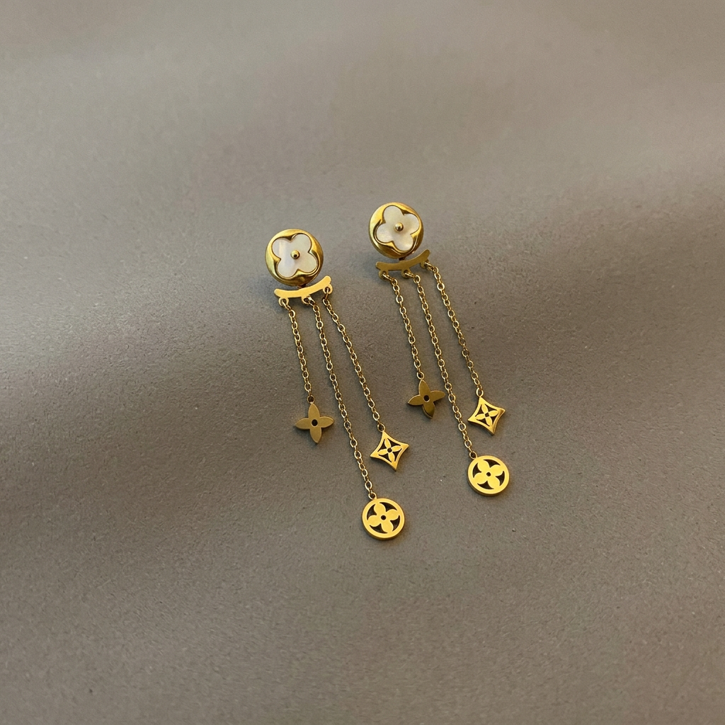 Gold mother-of-pearl clover ear-jacket earrings with three dangling chains on a warm-gray background.