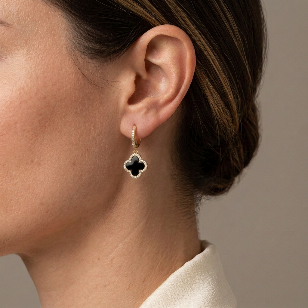 Close-up of a model wearing a black four-leaf clover drop earring with a crystal border and gold hoop.