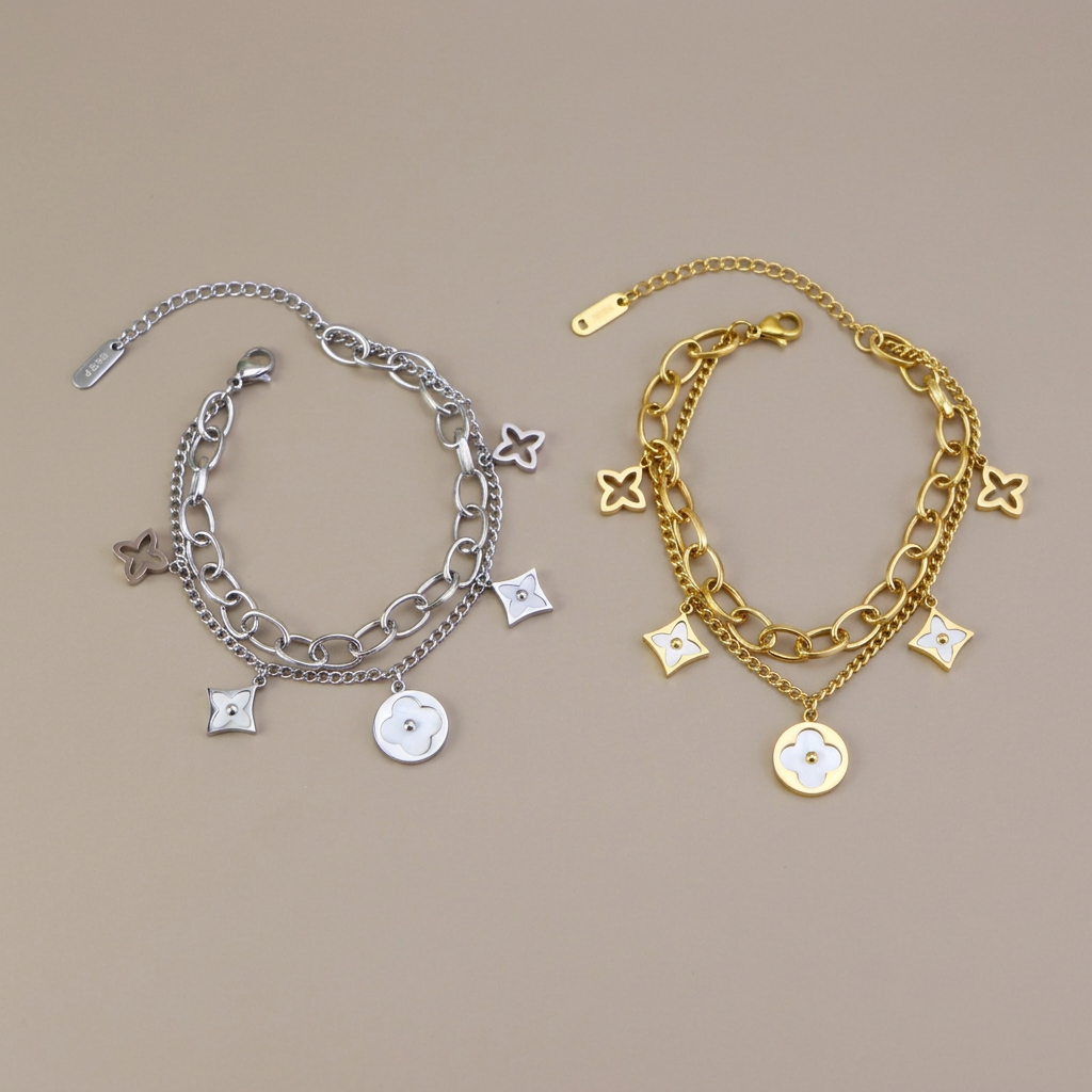 Silver and gold double-layer mother-of-pearl clover bracelets side by side on a warm-gray background.