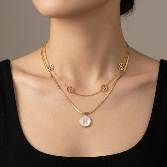 Model wearing a double-layer gold necklace with openwork H medallions and a mother-of-pearl H pendant.