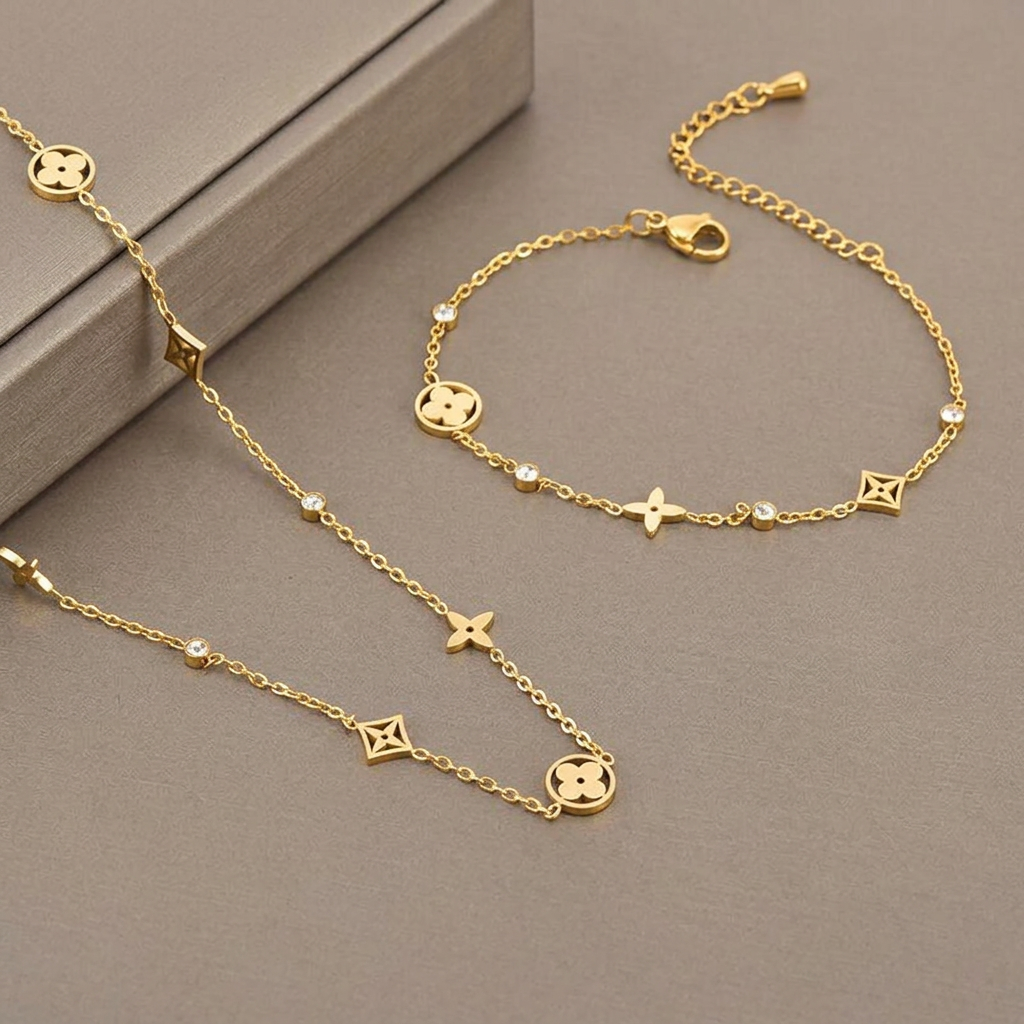 Gold clover necklace and matching bracelet displayed on a warm-gray studio background.
