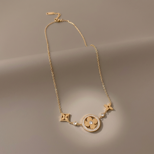 Gold clover necklace with CZ accents and flower charms on a warm-gray studio background.