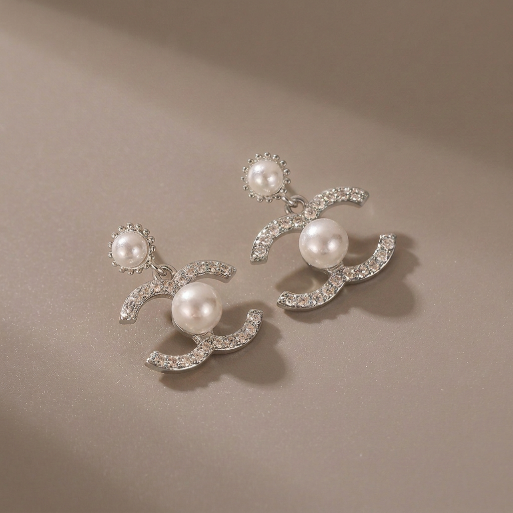 Silver double-C crystal and pearl earrings on a warm-gray background.