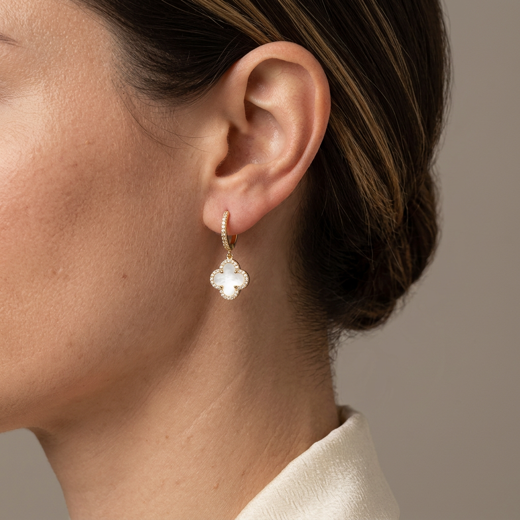 Close-up of a model wearing a white four-leaf clover drop earring with a crystal border and gold hoop.