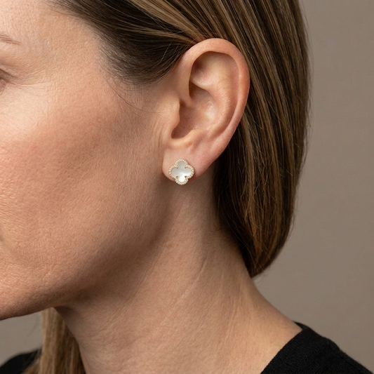 Close-up of a model wearing a white four-leaf clover stud earring with a clear crystal border.