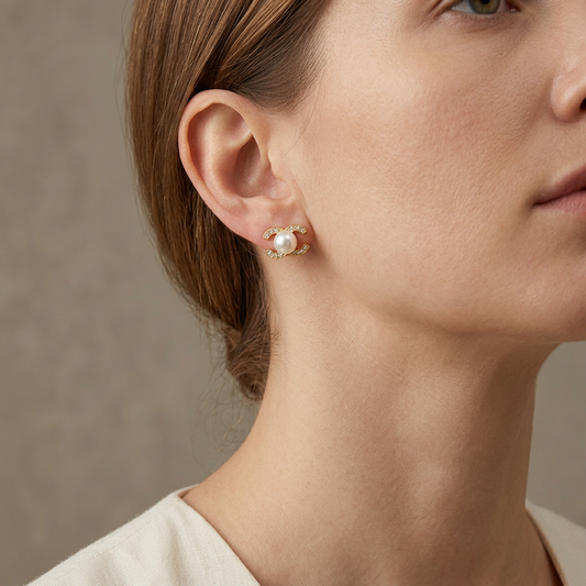 Close-up of a model wearing a gold crystal-set freshwater pearl stud earring against a warm-gray background.