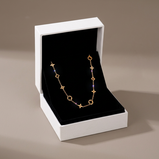 Gold clover necklace displayed in its open jewelry box against a warm-gray background.
