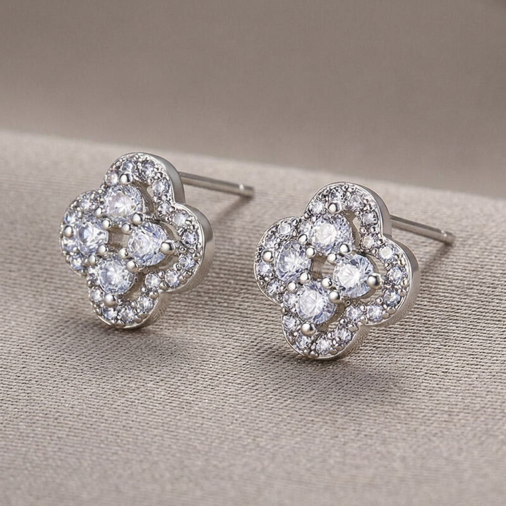 Angled view of platinum-colored crystal clover stud earrings on a warm-gray background.