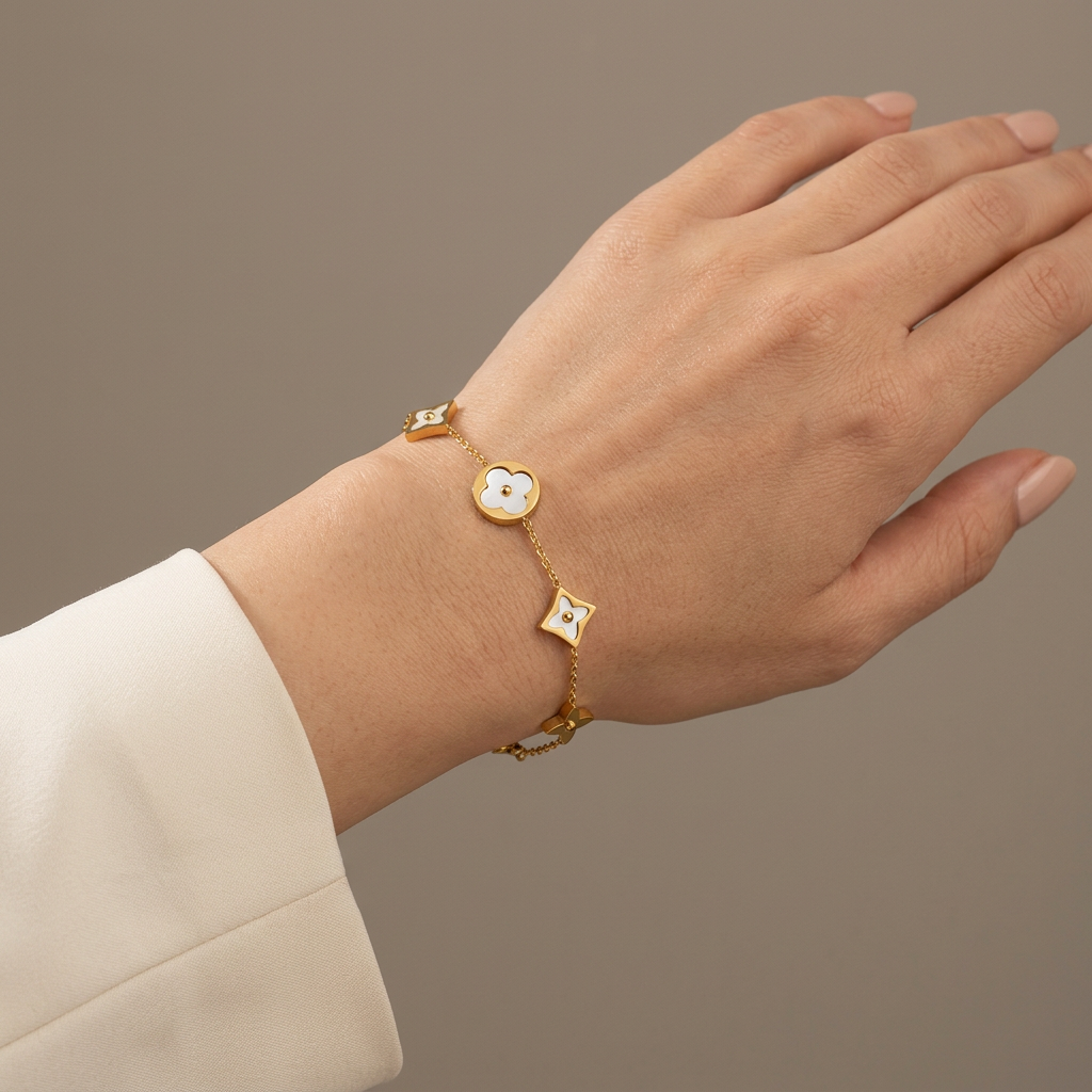Gold mother-of-pearl clover bracelet worn on a model’s wrist against a warm-gray studio background.