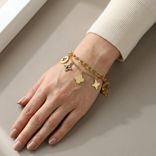 Model wearing a gold double-chain bracelet with dangling clover and star charms.