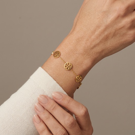 Gold Double T medallion bracelet worn on a model’s wrist against a warm-gray studio background.