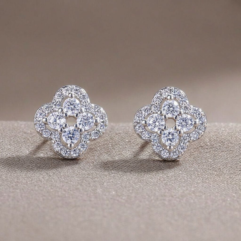 Front view of platinum-colored crystal clover stud earrings on a warm-gray background.