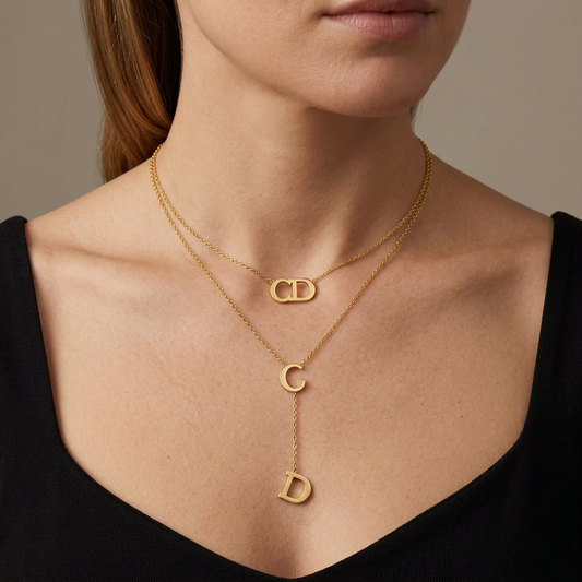 Model wearing a gold double-layer necklace with an upper CD pendant and a lower C pendant with a D chain drop.
