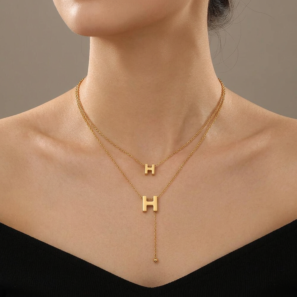 Model wearing a double-layer gold H necklace with two H pendants and a dangling chain tail.