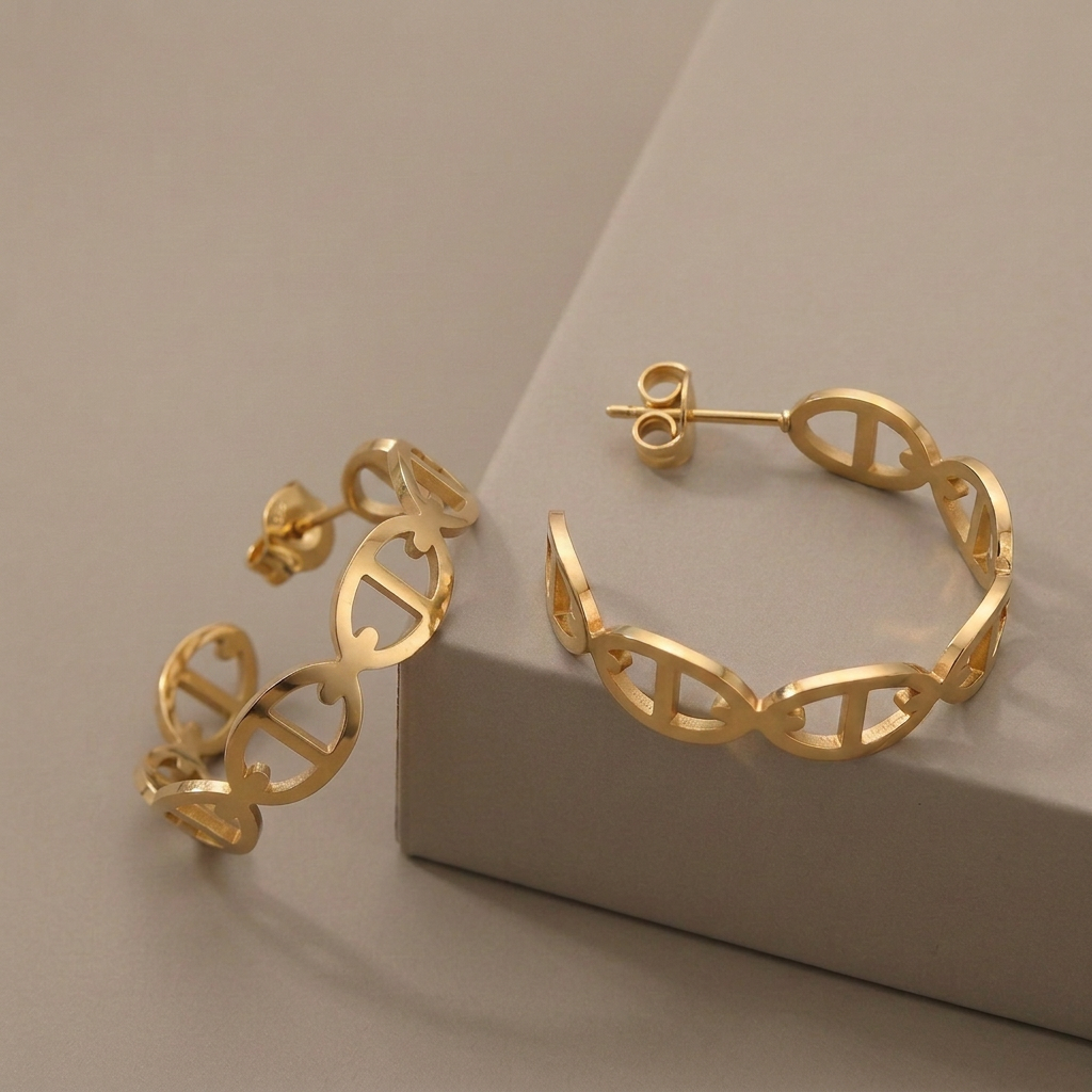Gold D-motif hoop earrings with butterfly backs arranged against a warm-gray display block.