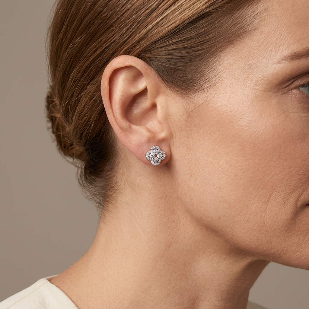 Close-up of a model wearing a platinum-colored crystal clover stud earring against a warm-gray background.