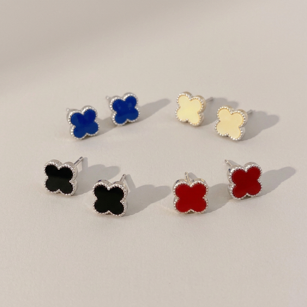 Four pairs of silver-tone clover stud earrings in pale cream yellow, blue, red and black on a warm gray background