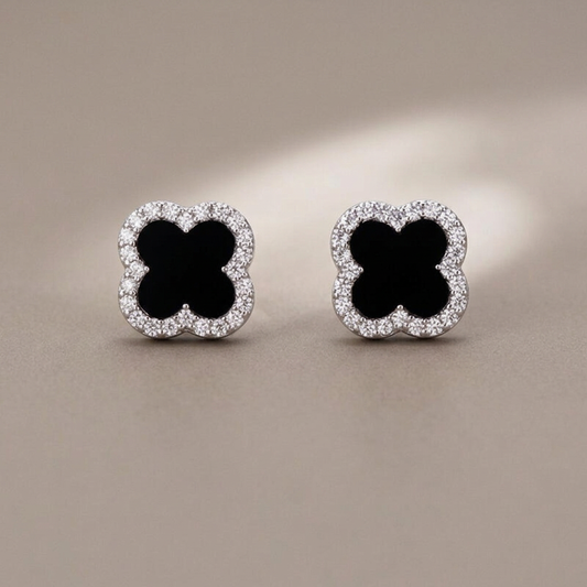 Black clover CZ stud earrings on a warm gray background