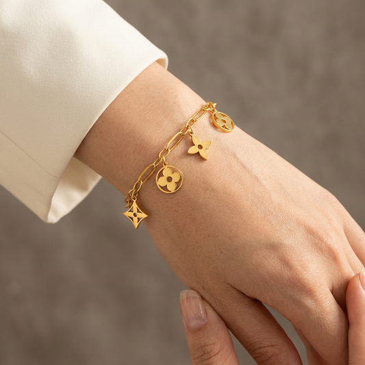 Close-up of a wrist wearing a gold paper-clip chain bracelet with five flower and openwork charms.