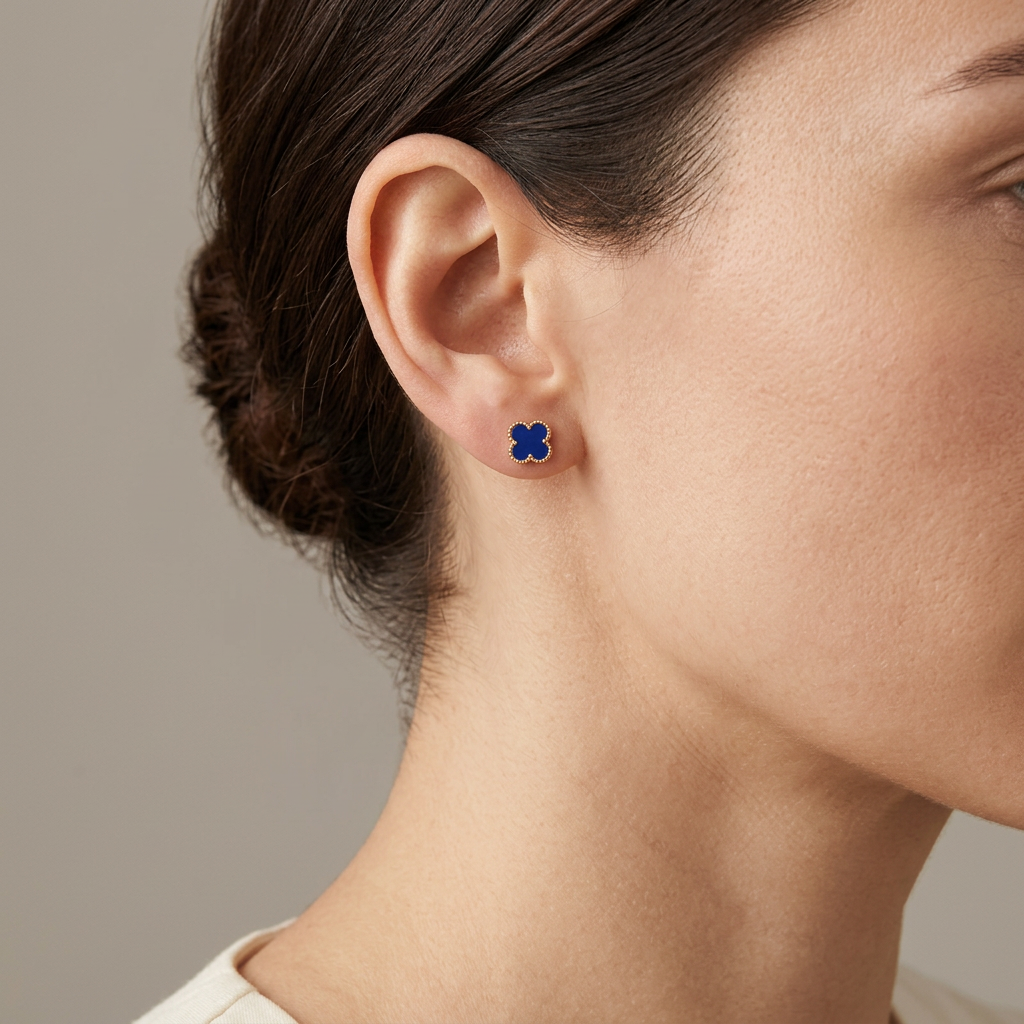 Blue clover stud earring with gold-tone beaded edging worn by a model against a warm gray background